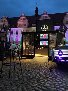 frontaler Blick auf Stand, beleuchtetes Fahrzeug mit dem Mercedes-Benz Event Cube im Hintergrund