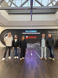 F&uuml;nf Personen stehen nebeneinander f&uuml;r ein Gruppenfoto vor einer gro&szlig;en Medienwand. Auf dem Bildschirm hinter ihnen leuchtet der Schriftzug Willkommen zusammen mit dem Logo von Ehrlich Logistics