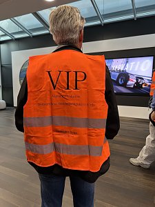 Ein Mann von hinten gesehen tr&auml;gt eine leuchtend orangefarbene Warnweste mit der gro&szlig;en Aufschrift VIP. Im Hintergrund ist ein Bildschirm zu erkennen, auf dem ein Lkw abgebildet ist.