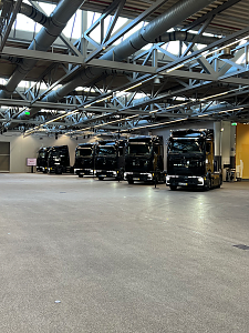 Eine ganze Reihe fabrikneuer, gl&auml;nzend schwarzer Mercedes-Benz Lkw steht nebeneinander aufgereiht in einer riesigen Werkshalle.