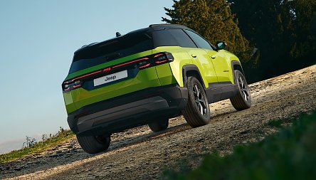 Der neue Jeep&reg; Compass e-Hybrid - Gr&uuml;ner Jeep Compass von hinten, f&auml;hrt leicht bergauf auf einem Schotterweg, B&auml;ume im Hintergrund.