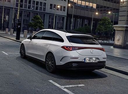 Das Bild zeigt einen weißen Mercedes-Benz CLA Shooting Brake, der auf einer breiten, nahezu leeren Stadtstraße steht. Moderne Gebäude umgeben die Szene. Der Wagen ist von hinten, seitlich zu sehen und vermittelt Dynamik sowie Eleganz.