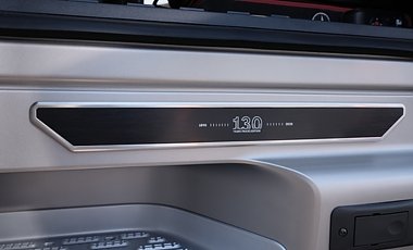 Nahaufnahme einer Lkw-Plakette. Ein schmales, schwarzes Metallelement mit silberner Umrandung ist in die silberne Karosserie eingelassen. In der Mitte steht die wei&szlig;e Zahl 130, flankiert von kleiner Schrift und feinen Linie.